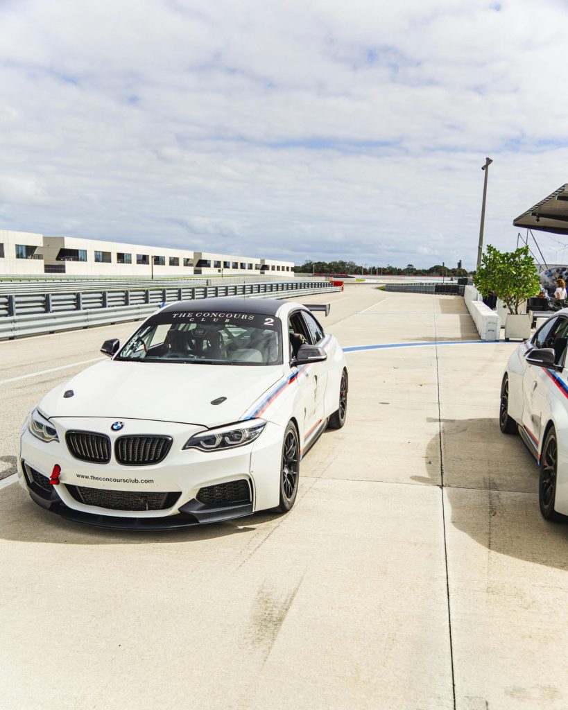Two white sports cars parked on a race track under a cloudy sky, ready for a race.